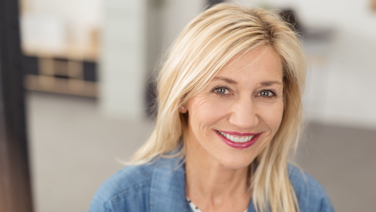 Long-haired blond woman with a joyful facial expression smiling at camera with blue eyes and white teeth, portrait indoors.