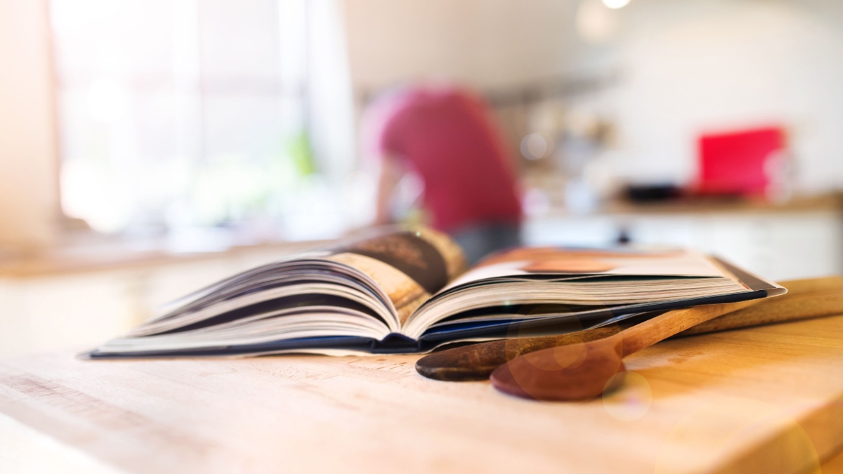 Cook book laid on a kitchen table with two wooden spoons