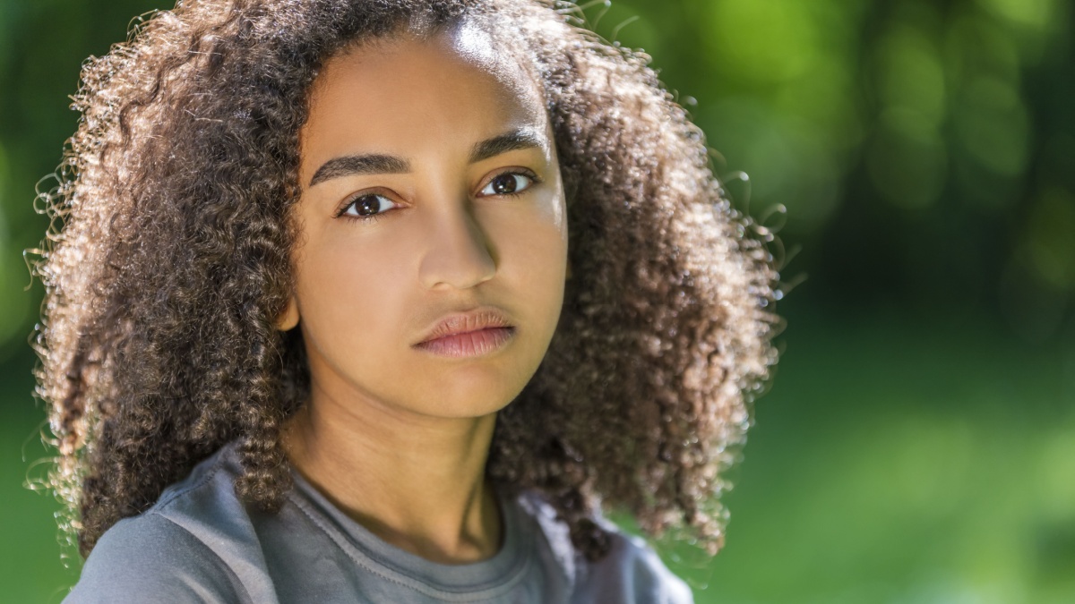 Beautiful mixed race African American girl teenager female young woman outside in spring or summer looking sad depressed or thoughtful.