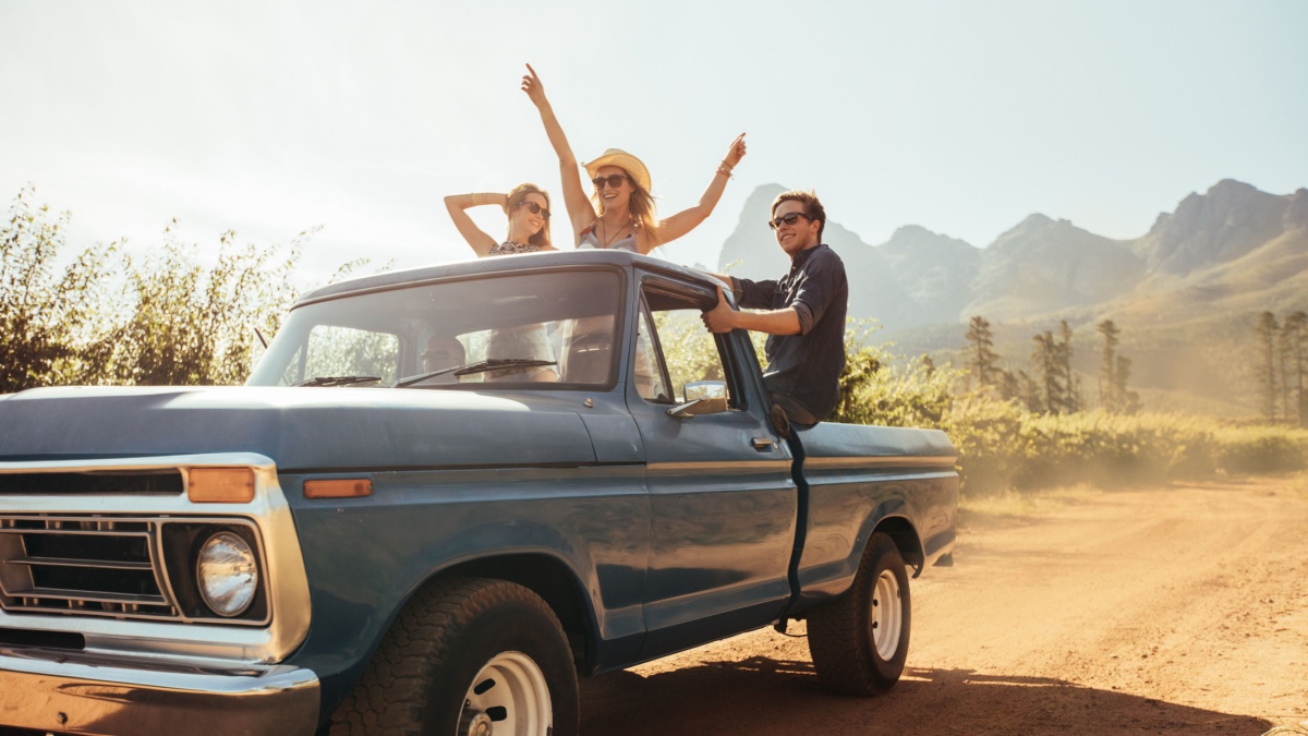 Group of people at the back of a pick up truck having fun. Young men and women enjoying on a road trip in countryside on a sunny day.