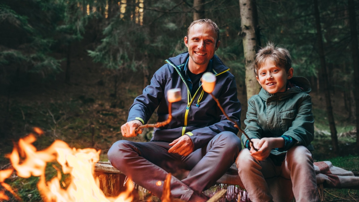 Father and son roast marshmallow candies on the campfire in forest. Spring or autumn camping