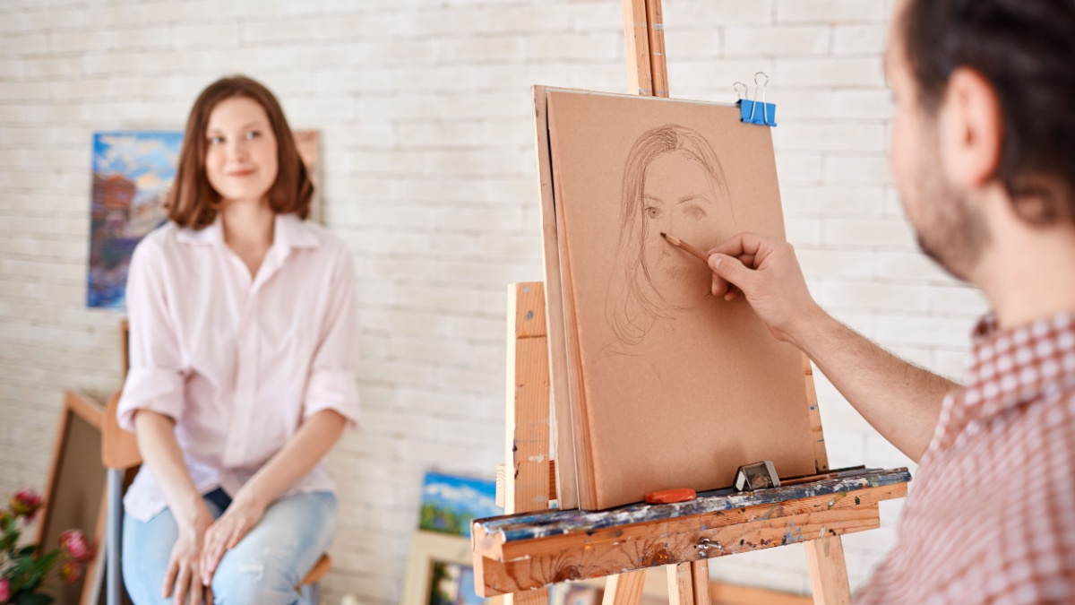 Back view portrait of artist sketching models portrait in art workshop, focus on the picture in pencil