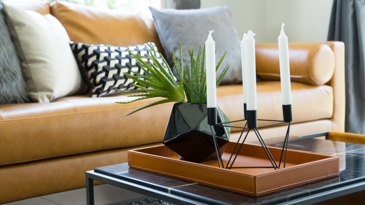 Brown leather sofa near a coffee table with black vase and modern candle holder.