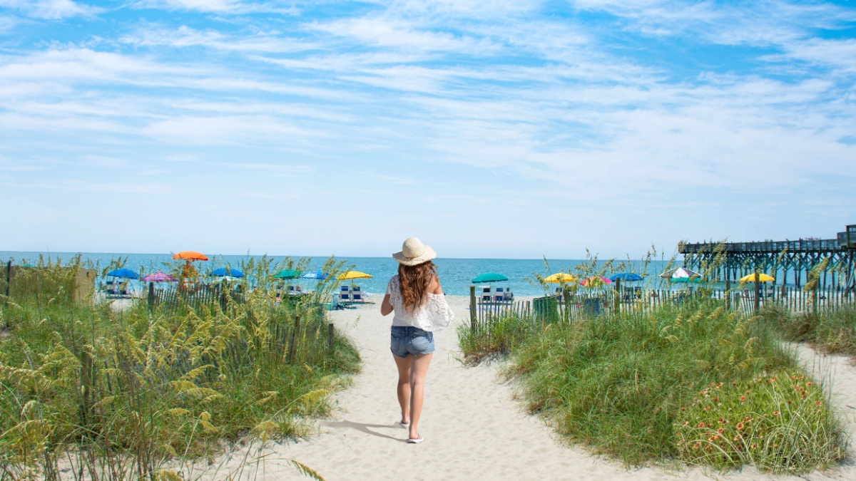 Girl walking on the beach on summer vacation. Beach chairs and parasols on sand in the background. Myrtle Beach, South Carolina, USA.