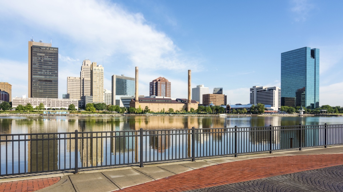 A panoramic view of downtown Toledo Ohio's skyline from across the Maumee river at a popular restaurant area with a paver brick boardwalk and a decorative iron railing..