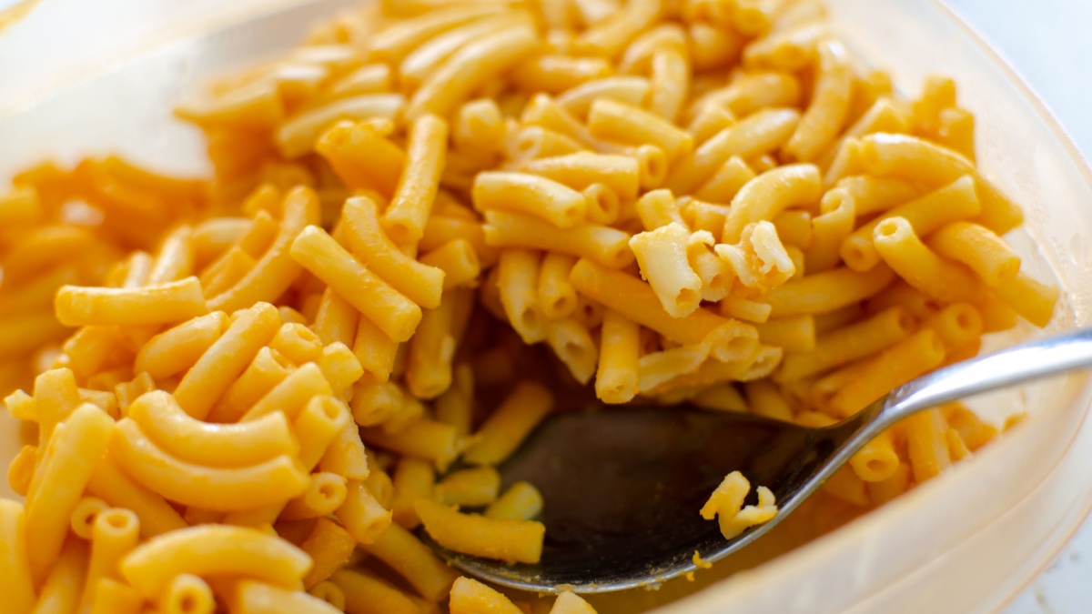 leftover bright orange kraft dinner macaroni and cheese being spooned for reheating