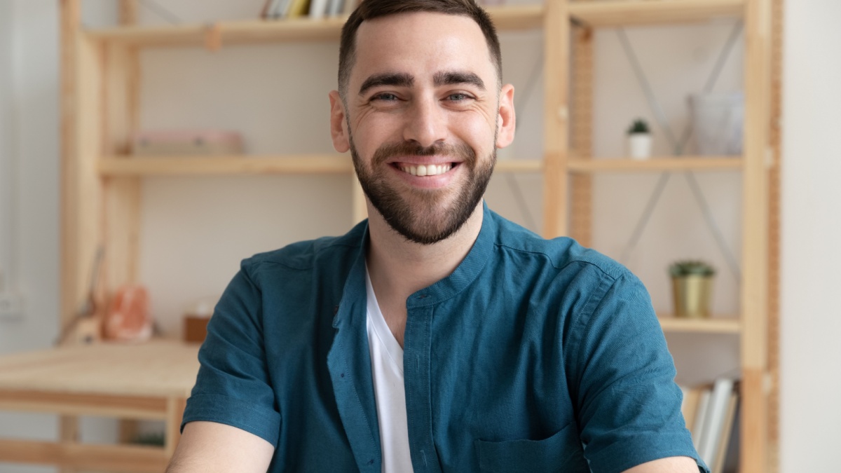 Headshot portrait of smiling Caucasian young male employee look at camera posing at workplace, happy European businessman show confidence.