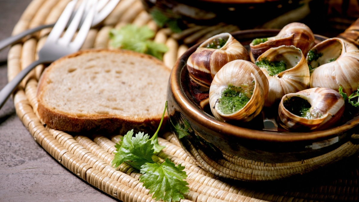 Escargots de Bourgogne - Snails with herbs butter, gourmet dish, in two traditional ceramic pans with coriander and bread on straw napkin.