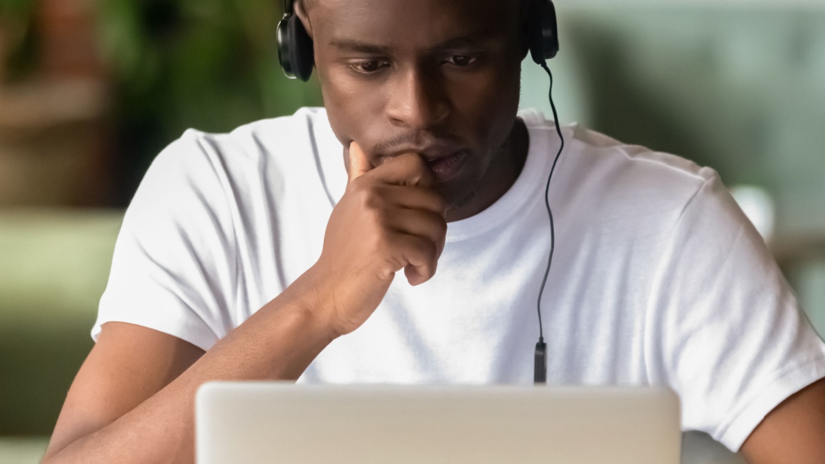 Focused African student wear headphones studying on-line do exercise using laptop, watching video.
