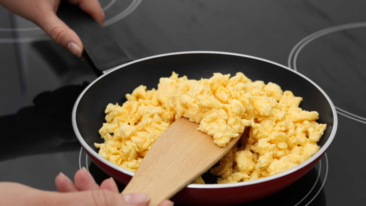 Woman cooking tasty scrambled eggs in frying pan on stove