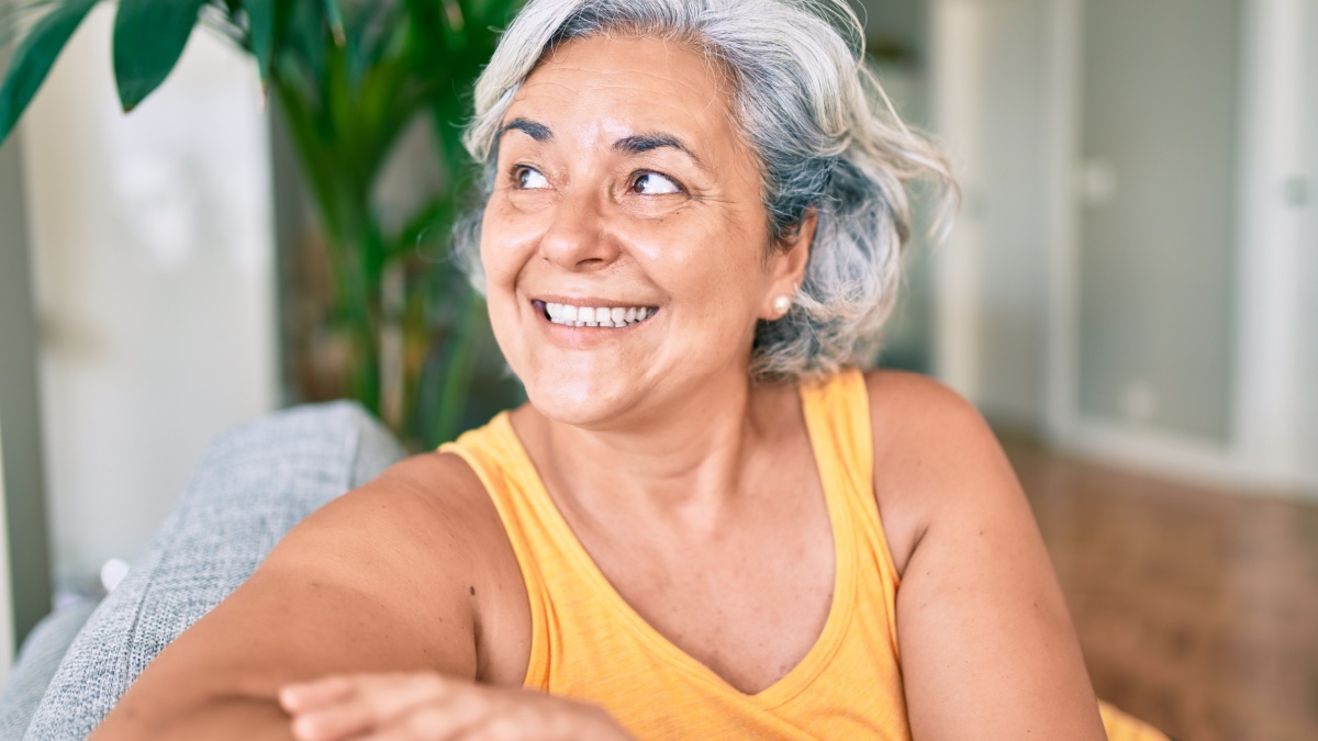 Middle age woman with grey hair smiling happy relaxing sitting on the sofa at home.