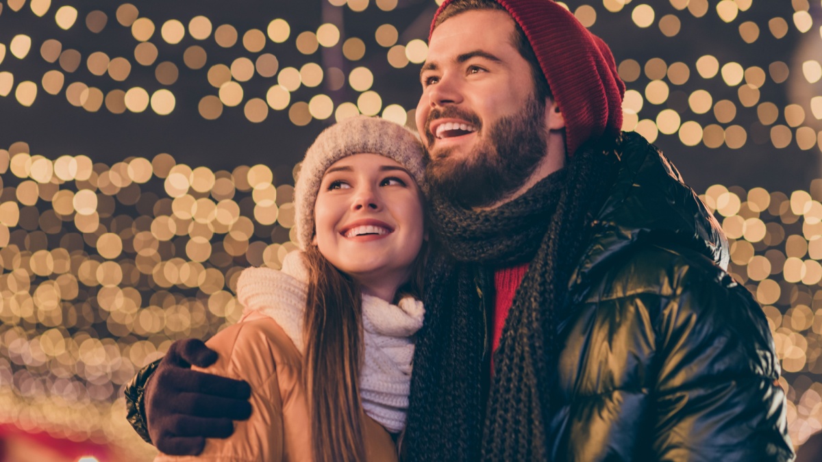 Photo of affectionate boyfriend hug girlfriend look enjoy x-mas tradition, illumination evening outside wear season coat scarf headwear.