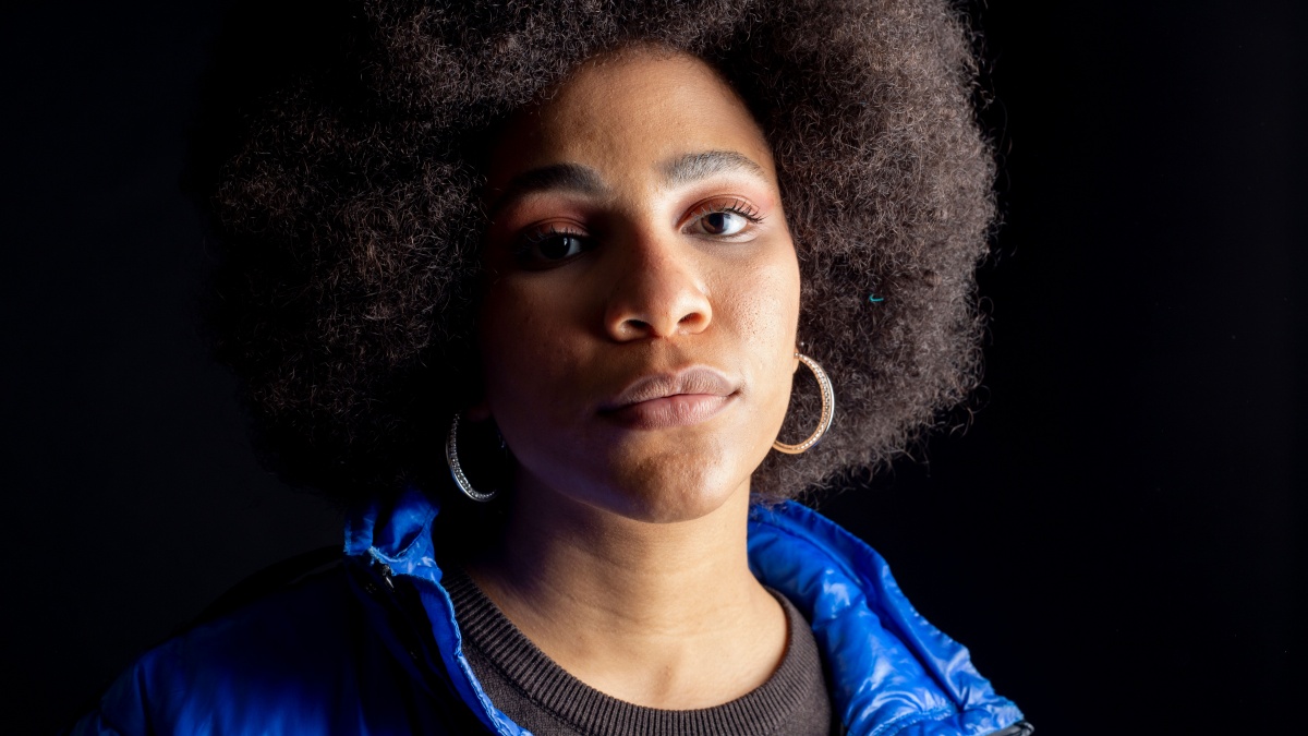 afro american woman, mixed race, posing on dark background, urban clothes, modern pretty and smiling.