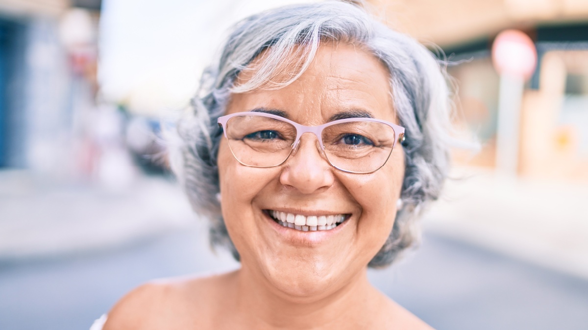 Middle age woman with grey hair smiling happy outdoors.