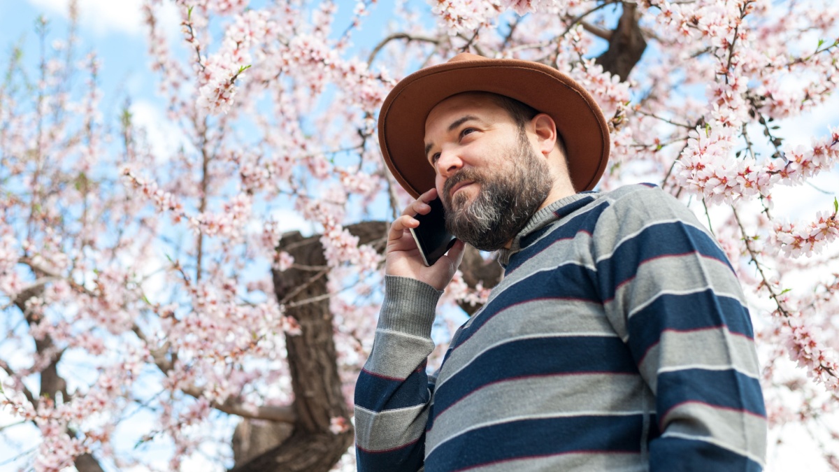 Man using smartphone next to a blooming pink tree. Spring and technology concept.