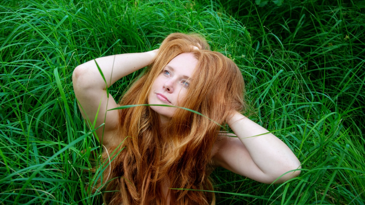 Portrait of a beautiful sexy elder, mature redhead content, satisfied woman looking up to the sky, in the spring green grass.