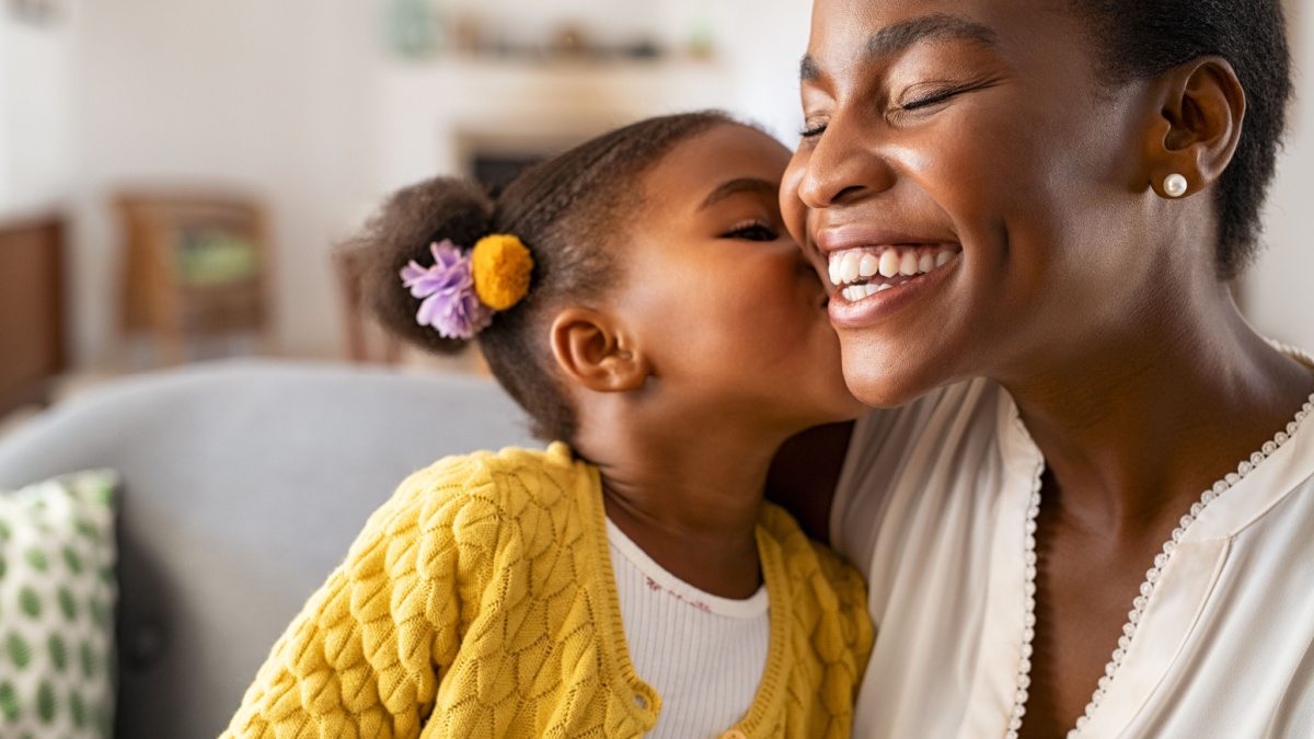Close up of beautiful daughter kissing mother on cheek at home.