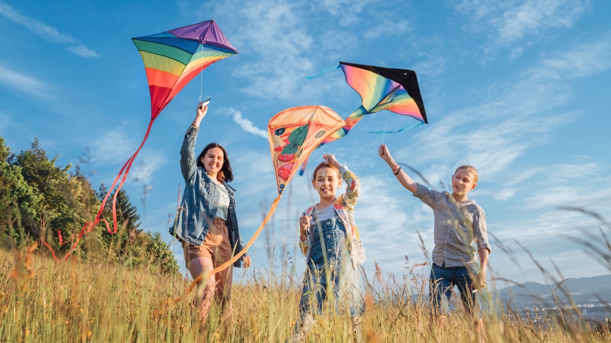 Smiling gils and brother boy running with flying colorful kites on the high grass meadow in the mountain fields.