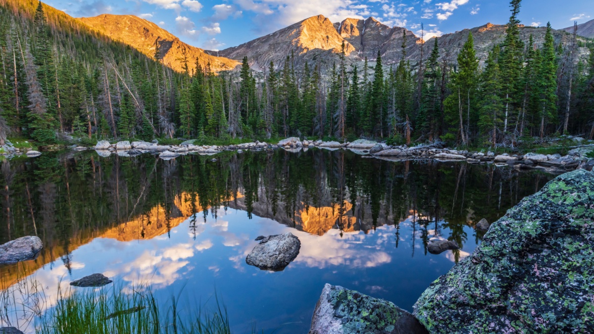 Boulders surround the calm water of Chipmunk Lake reflecting Ypsilon Mountain and Mount Chiquita lit by morning light in Rocky Mountain National Park.