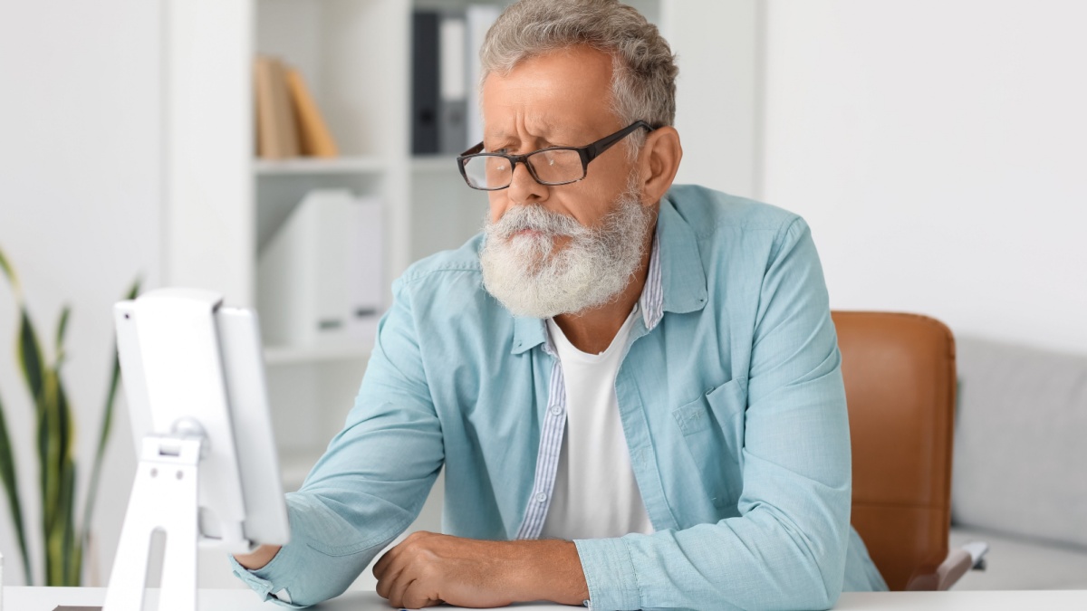 Senior bearded man using tablet computer at table in office.