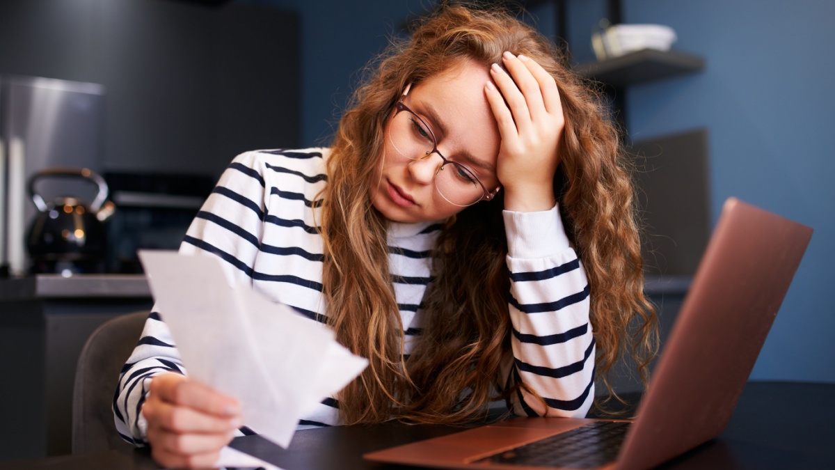 Unhappy woman calculates expenses on bills, upset about increased utilities prices. Female counting paychecks, debts, loans, reciepts to pay taxes.