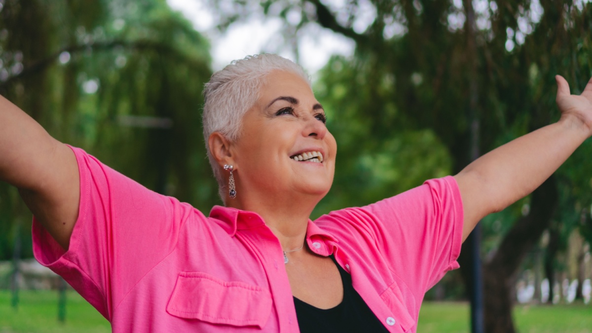 older gray haired latin woman with her arms outstretched in nature full of vitality.