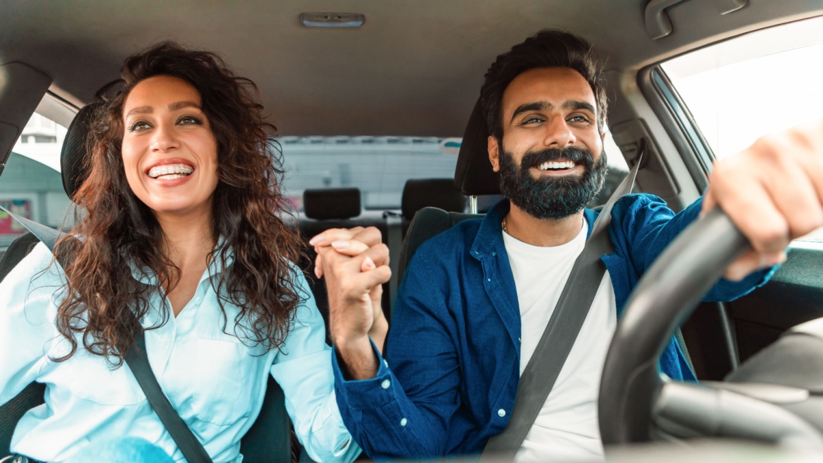 Happy middle eastern couple sitting in auto and holding hands, enjoying ride on front passenger and driver's seat.
