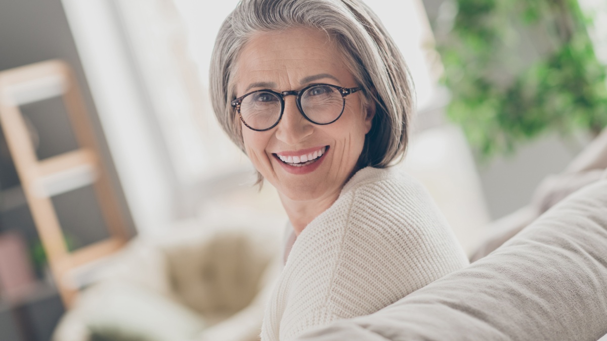 Photo of adorable pretty senior lady dressed white cardigan eyewear smiling indoors house room.
