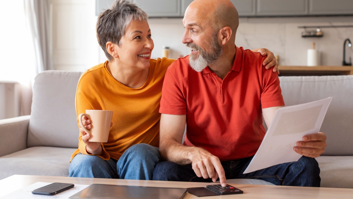 Happy Senior Spouses Checking Financial Documents And Calculating Family Budget At Home, Cheerful Elderly Couple Sitting At Table In Living Room.