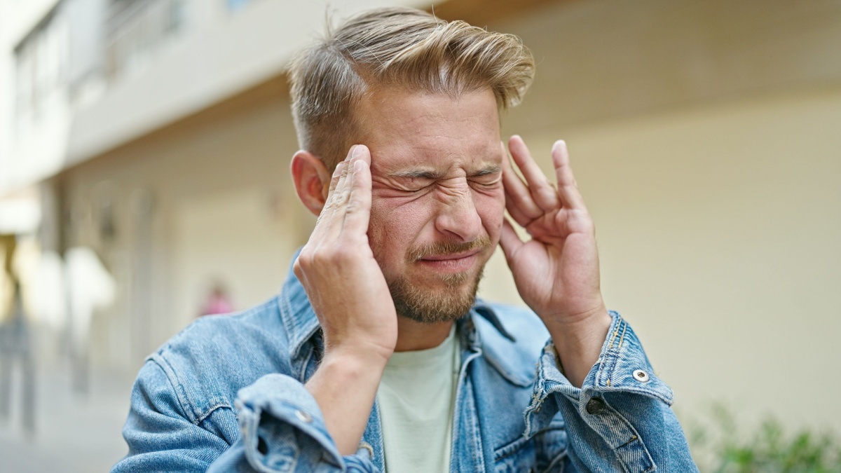 Young caucasian man suffering for headache at street.