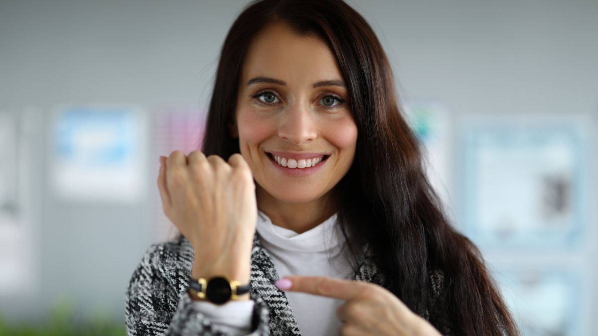 Close-up of smiling beautiful businesswoman pointing at wristwatch. Pretty young brunette woman in luxury costume. Time management and business.