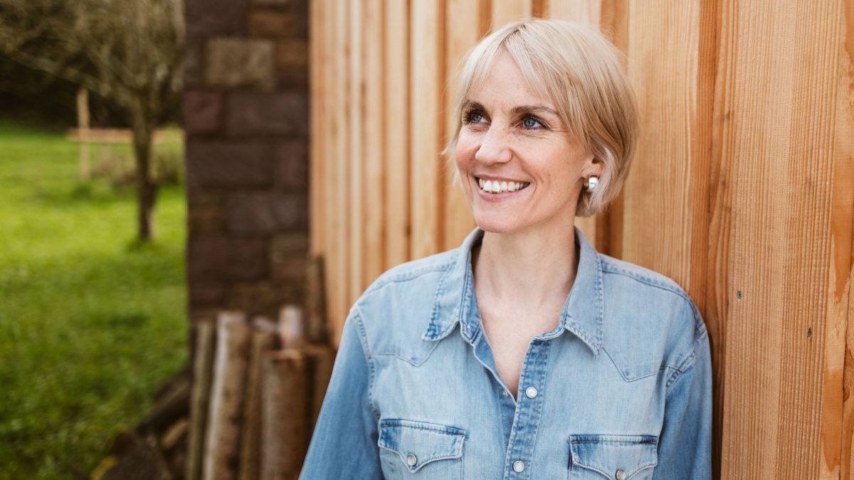 Smiling Woman in Denim Shirt Leaning Against Wooden Wall.
