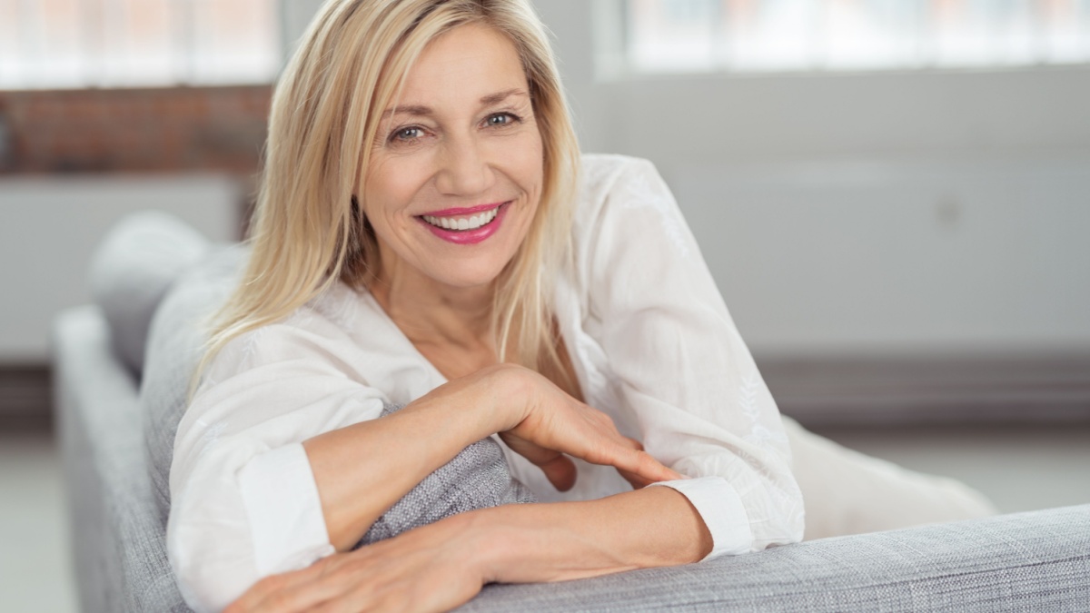 Close up Pretty Blond Adult Woman Sitting on Gray Couch, Looking at Camera with a Happy Facial Expression.