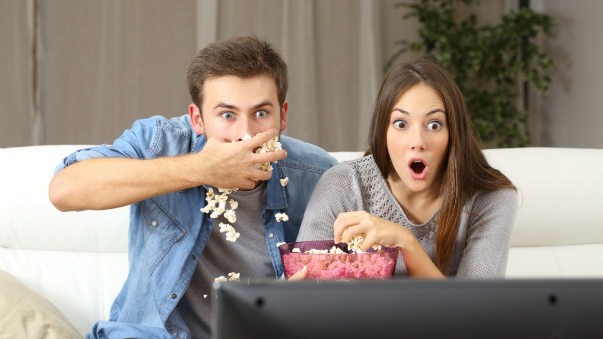 Amazed couple watching tv program sitting on a couch at home.