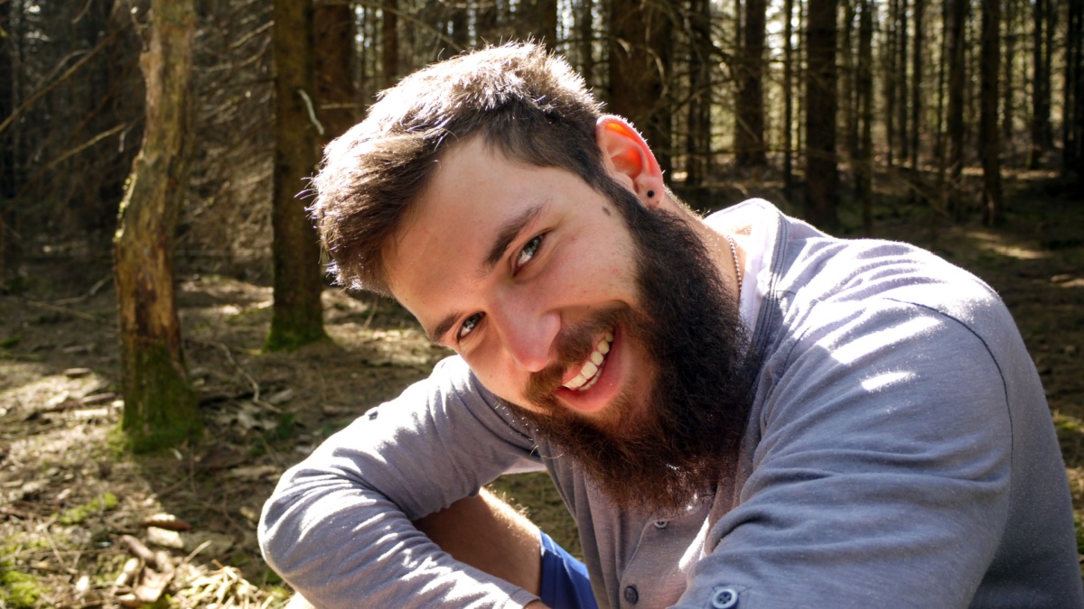 One happy, handsome man with a long beard sitting in the middle of a pine forest on a sunny day. Taken in Dentlein Am Forst, Germany.