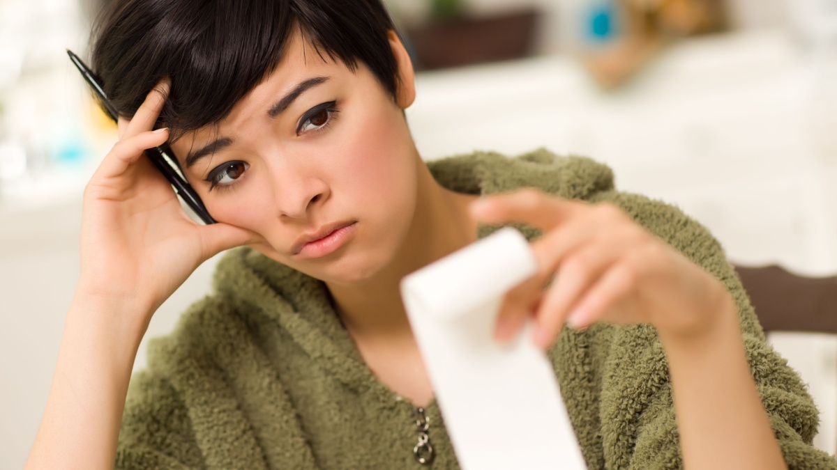 Multi-ethnic Young Woman Agonizing Over Financial Calculations in Her Kitchen.