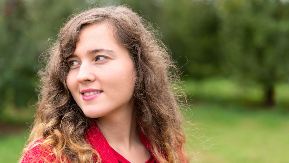 Apple orchard with many green trees park in garden bokeh background during autumn fall in farm countryside of Virginia with young happy woman in red dress portrait smiling.