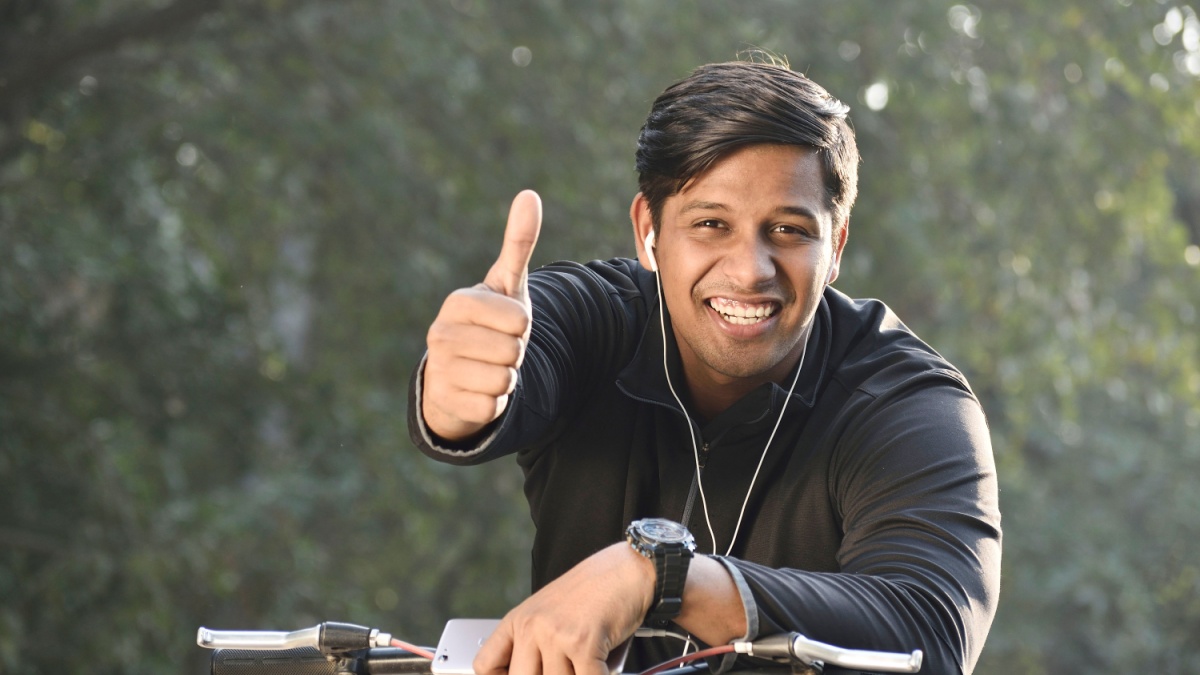 portrait of young Indian man sitting on cycle, showing thumbs up.