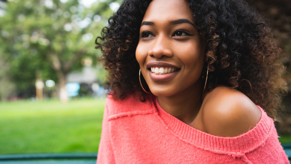 Portrait of young beautiful afro american woman sitting on bench in the park. Outdoors.
