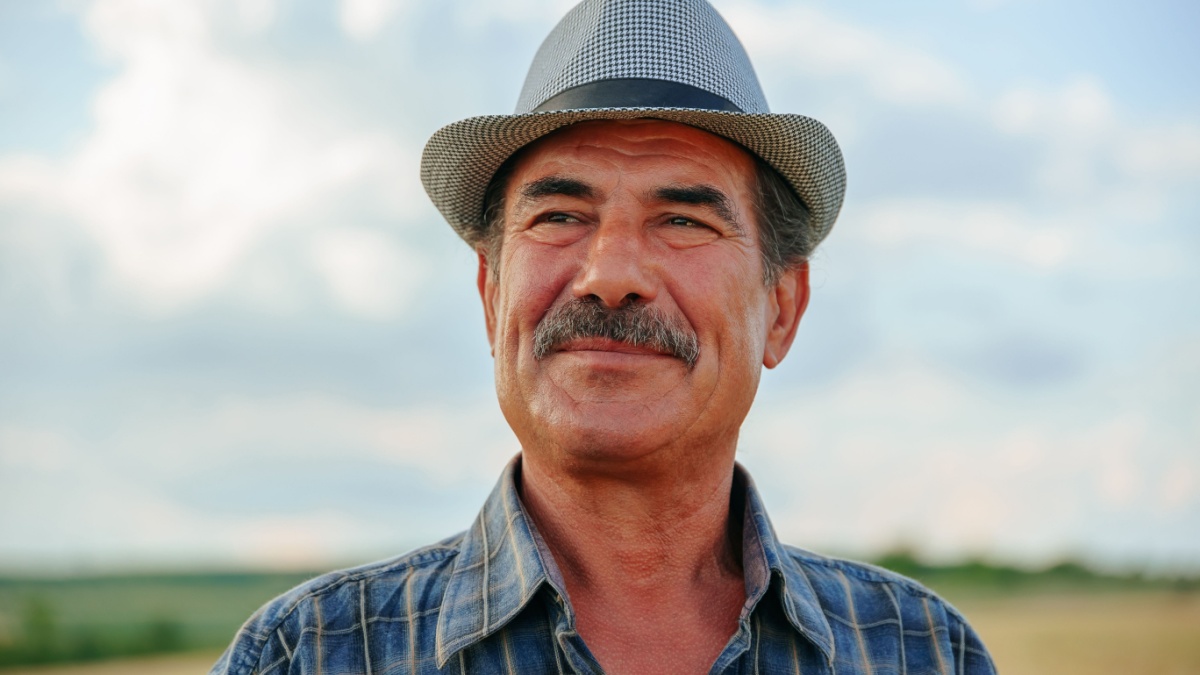 close up of a human head aged farmer with mustache against in the sky background. old male farmer worker with arms crossed. front view.