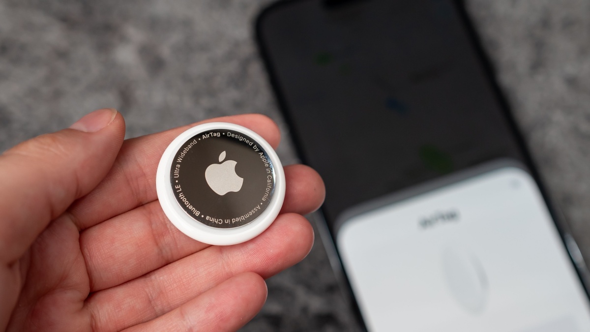 Jurmala, Latvia - 21 09 2023: In woman's hand small AirTag Apple, on background out of focus smartphone witch are connected to tag. Air Tag gadget to track of your stuff.