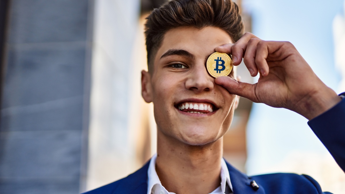 Young man wearing suit holding bitcoin over eye at street.