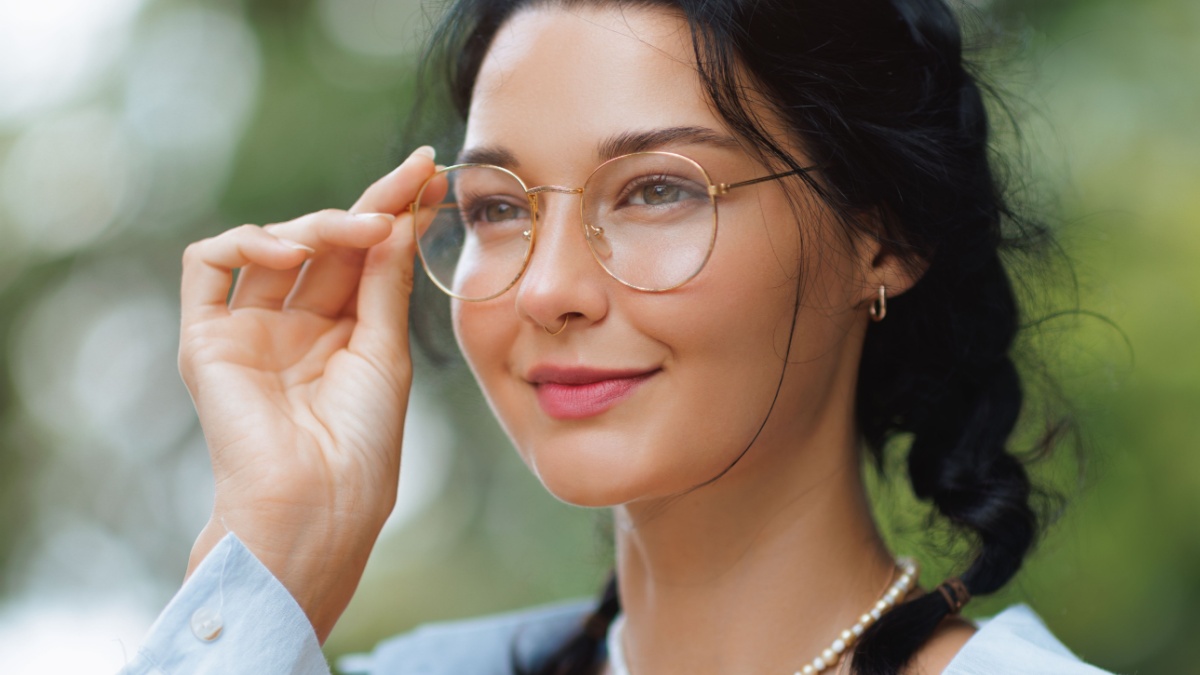 Stylish brunette woman wearing glasses, posing outdoors in a serene natural setting.