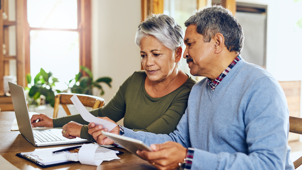 Senior couple, budget planning and health insurance checklist with computer at home. Documents, pension and elderly people with financial, tax and debt form in a house with bills and pc admin.